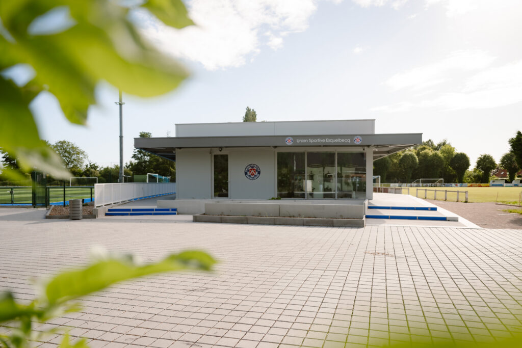 moderne betonnen clubhuis met terras en sportvelden van Union Sportive Esquelbecq