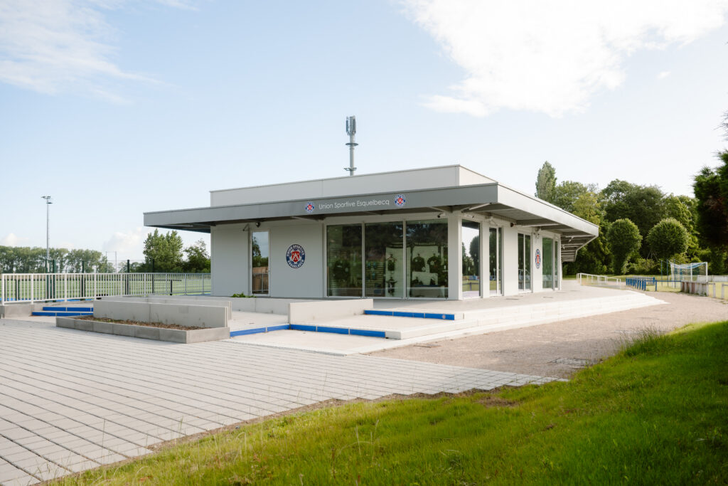 Modern prefab concrete clubhouse with large glass windows at sports complex in Esquelbecq