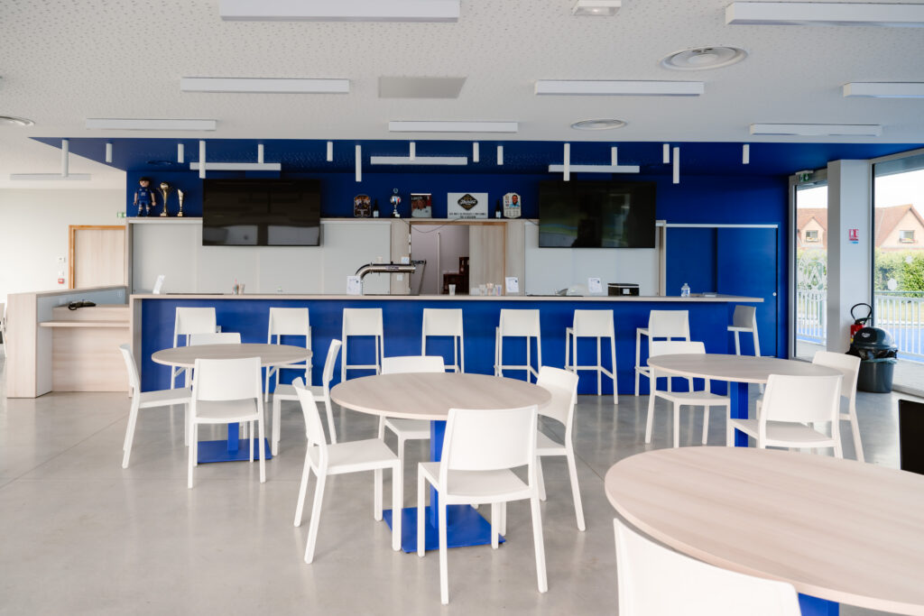 Interieur van moderne kantine met blauwe bar, witte stoelen en ronde tafels in industriebouw