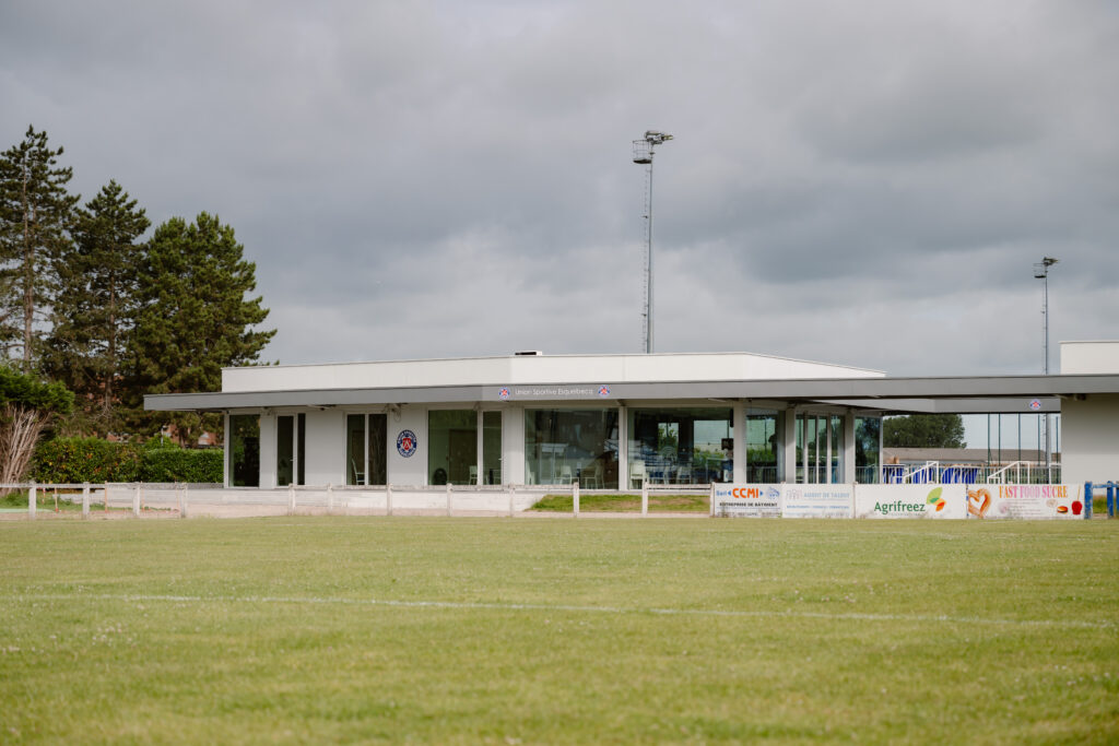 Modern prefab concrete sports club building with large windows and flat roof near soccer field