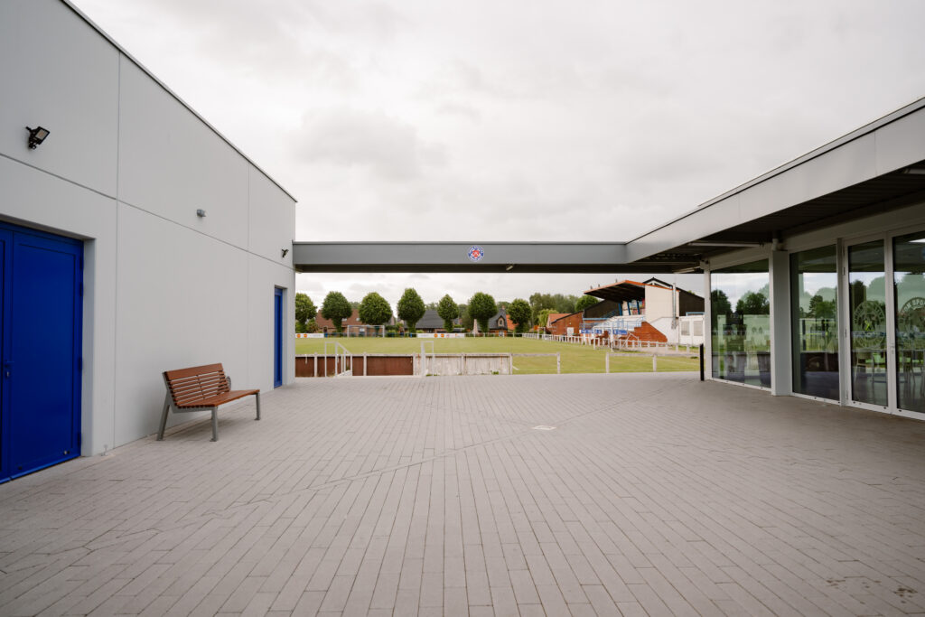 Modern industriebouw met prefab betonnen gevel en blauwe deuren naast sportveld